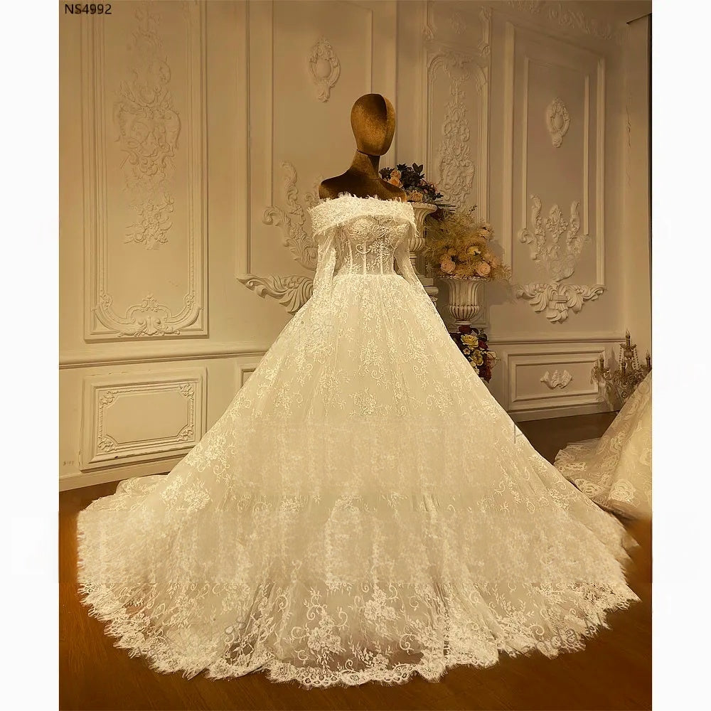 Three-quarter view of a graceful A-line wedding dress with sheer long sleeves and a voluminous lace-covered skirt.