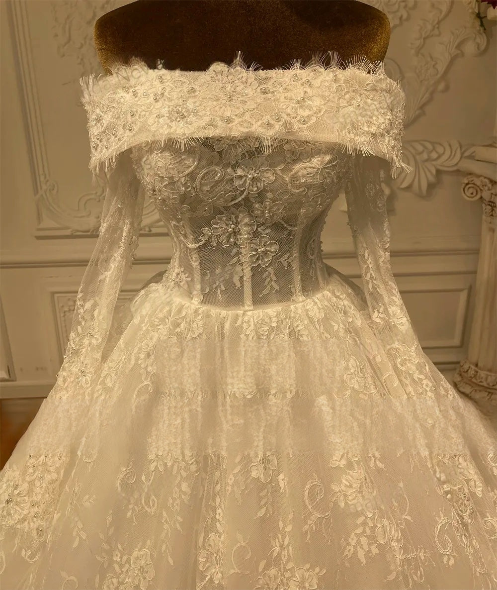 Close-up of a bridal gown's off-the-shoulder neckline and sheer bodice, showcasing detailed lace appliqués and scalloped edges.