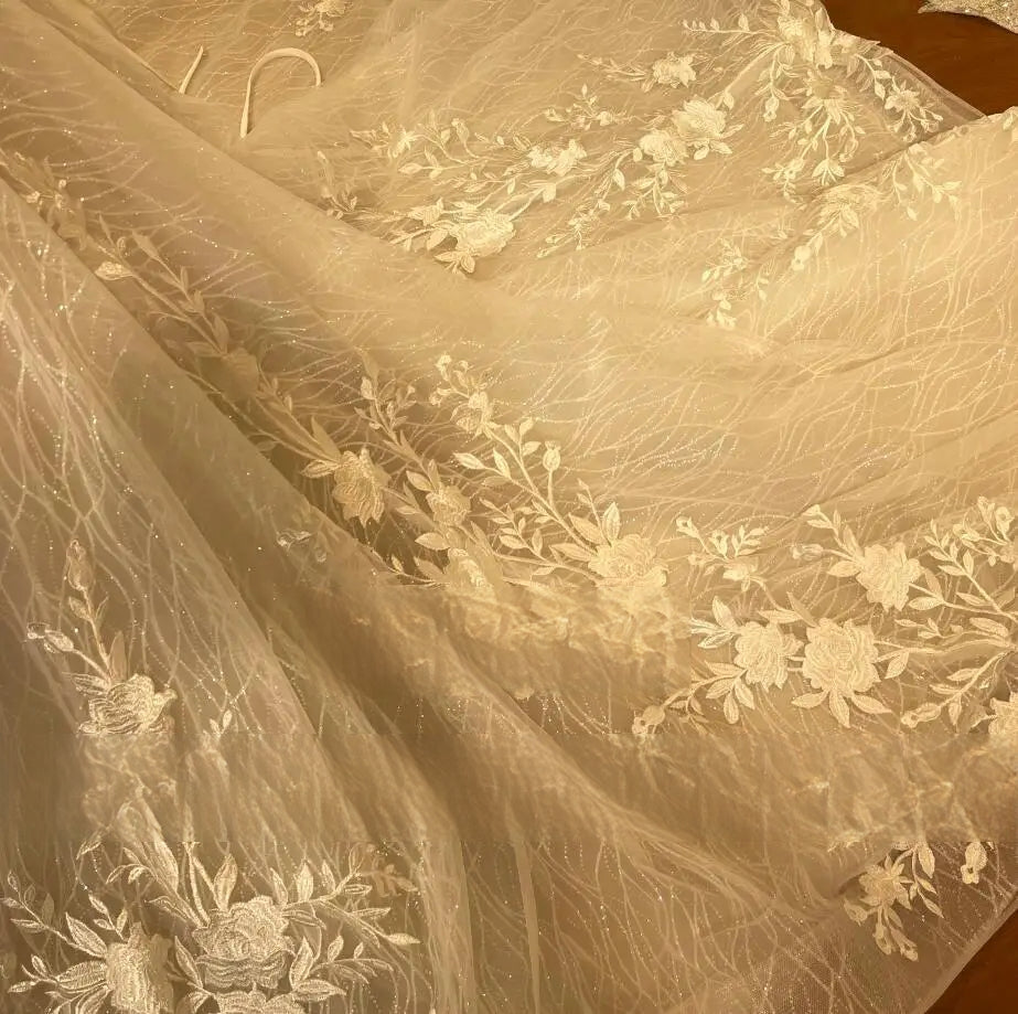 Close-up of the shimmering floral lace fabric and delicate embroidery on the skirt of a mermaid-style bridal gown.