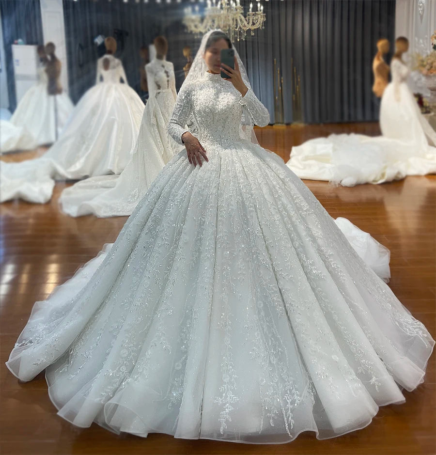 Full front view of a bride taking a selfie in a royal Islamic wedding dress, highlighting the sparkling, voluminous ball gown skirt and matching embellished bridal hijab.