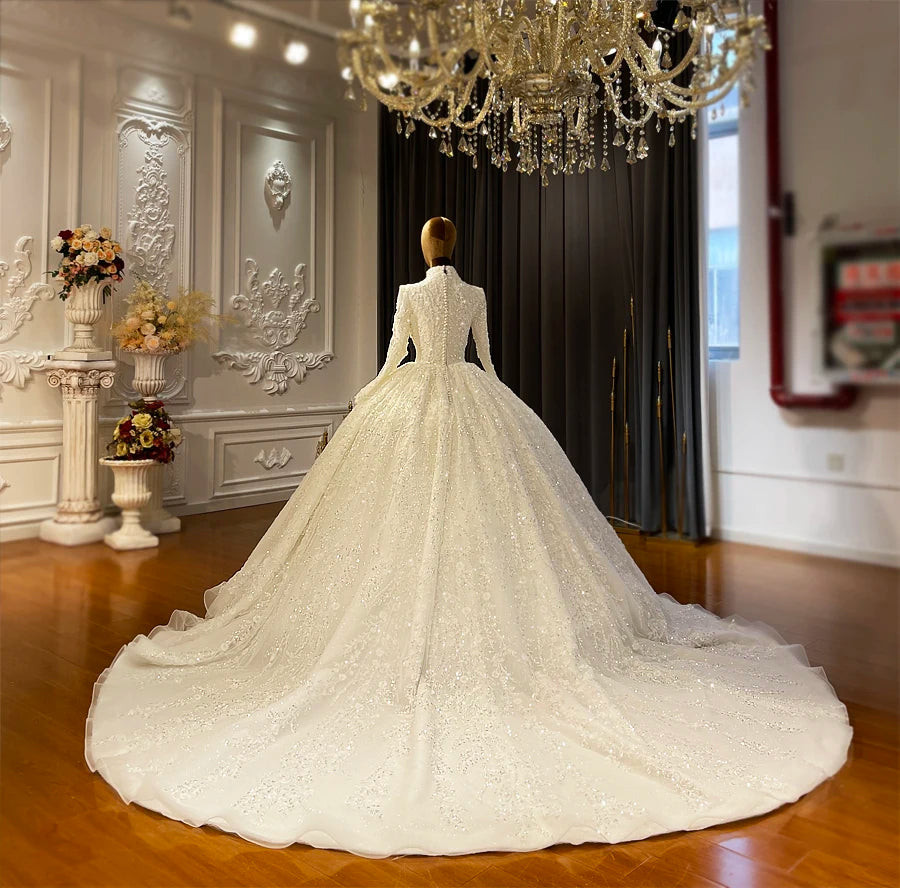 Rear view of a royal Islamic wedding dress on a mannequin, displaying the elegant row of back buttons and the expansive, shimmering cathedral-length train under a chandelier.
