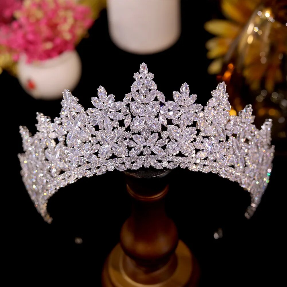 Front view of a brilliant silver cubic zirconia wedding crown displayed upright on a dark wooden stand against a black background.
