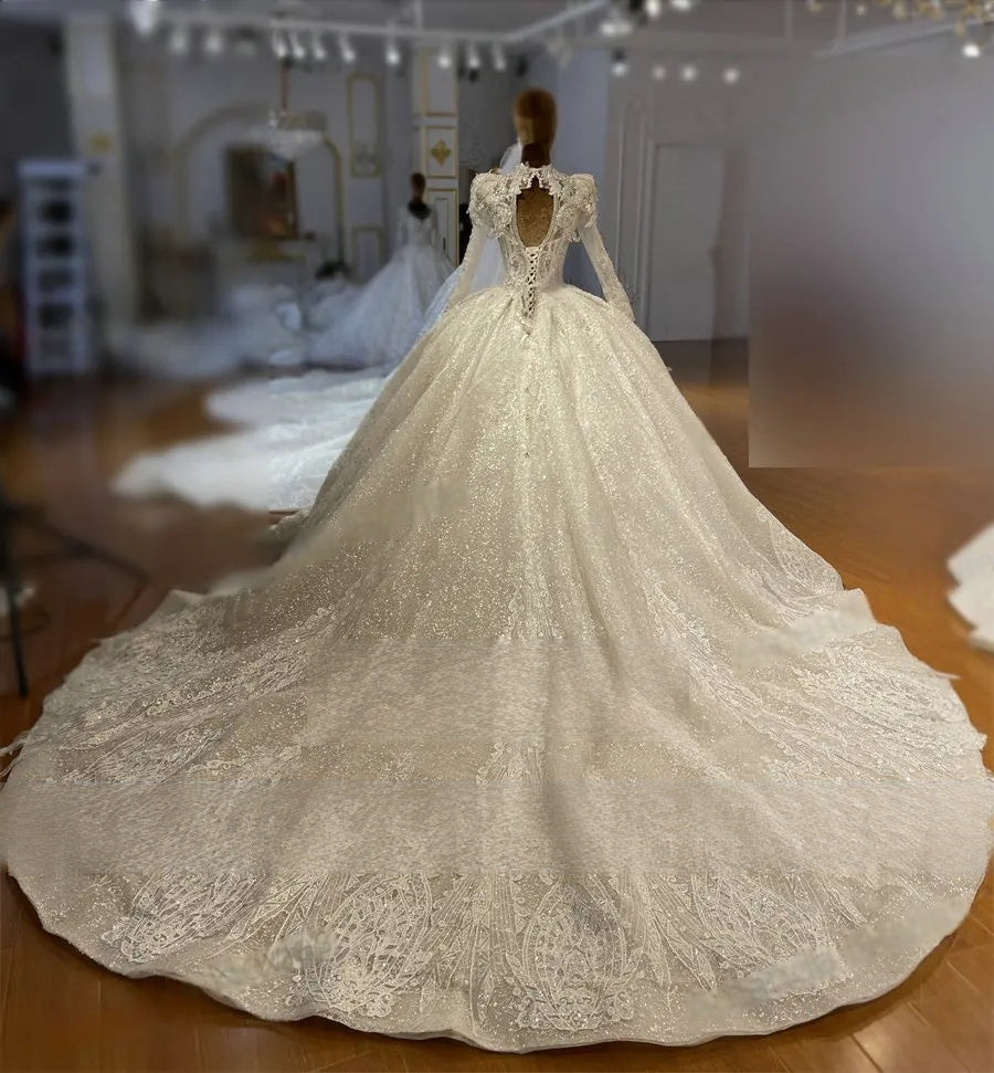 Back view of a long sleeve royal princess wedding gown on a mannequin, featuring an elegant keyhole back design, lace-up corset detail, and a wide lace-bordered train.