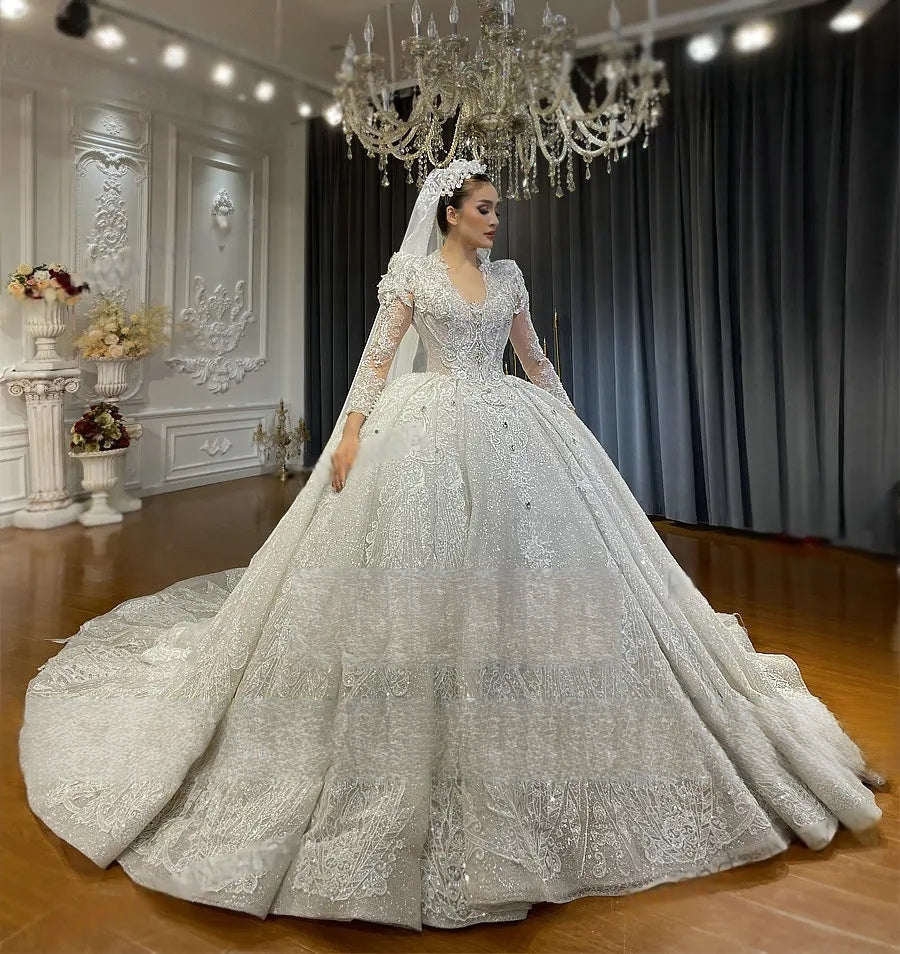 Side profile of a luxury V-neck princess wedding dress with long sleeves and a voluminous sparkling skirt, paired with a royal lace-edged bridal veil in a studio setting.