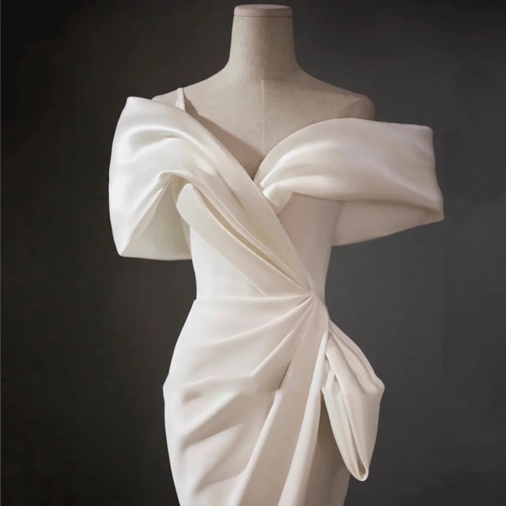Romantic pastel blush pink satin mermaid wedding gown featuring an architectural off-shoulder cuff collar and a dramatic thigh-high skirt slit.