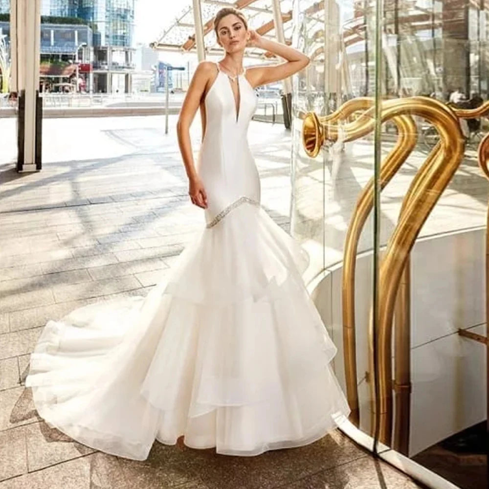 Simple white satin mermaid wedding dress featuring a halter neckline with a deep plunging keyhole slit, a beaded silver crystal waist trim, and a layered tulle trumpet skirt.