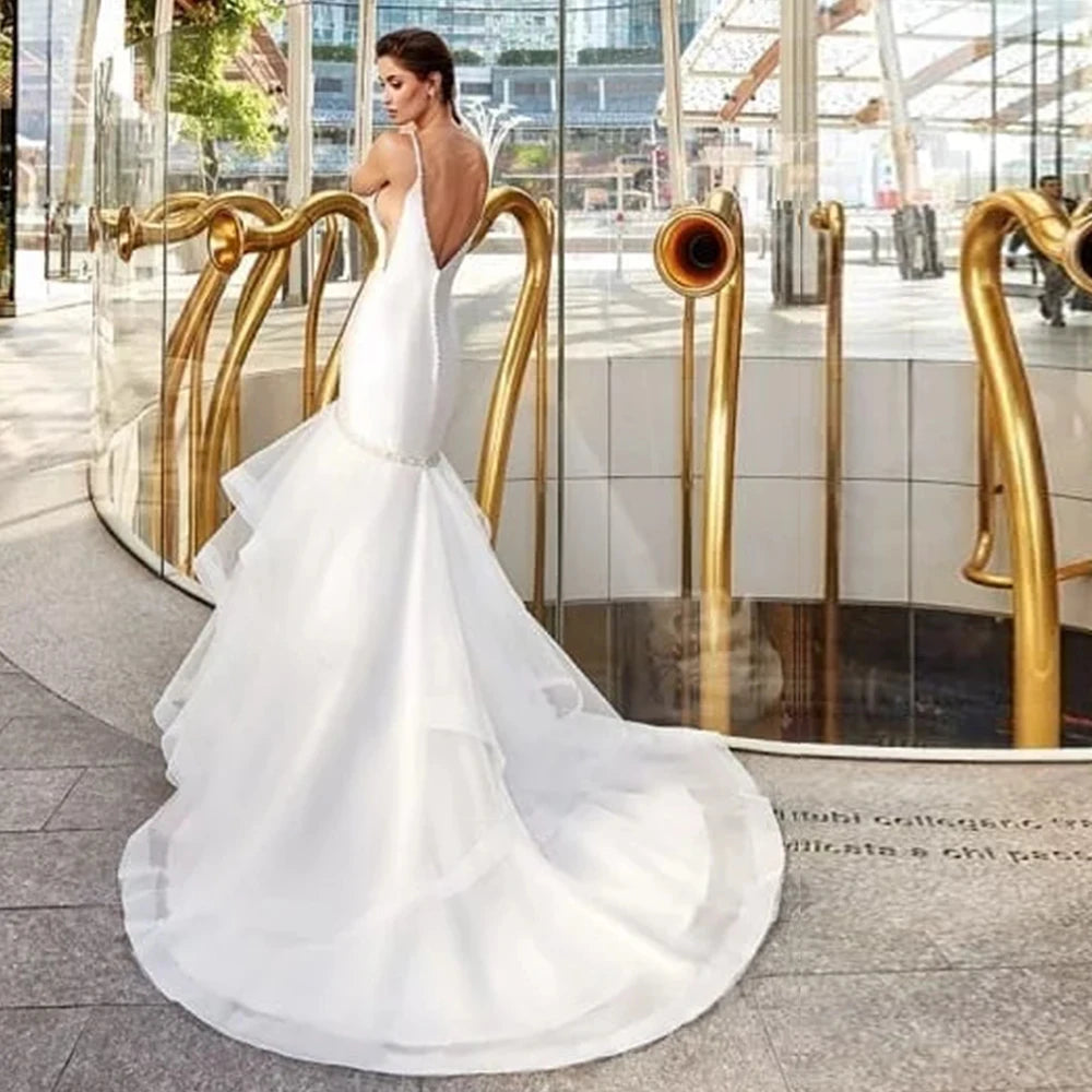 Rear view of a sexy backless satin bridal gown, showcasing an alluring low-cut open back, fabric-covered buttons down the zipper line, and a tiered tulle chapel train.