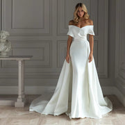 Minimalist satin mermaid wedding dress featuring a structured off-the-shoulder portrait collar, a plunging V-neckline, and a grand detachable satin overskirt train.
