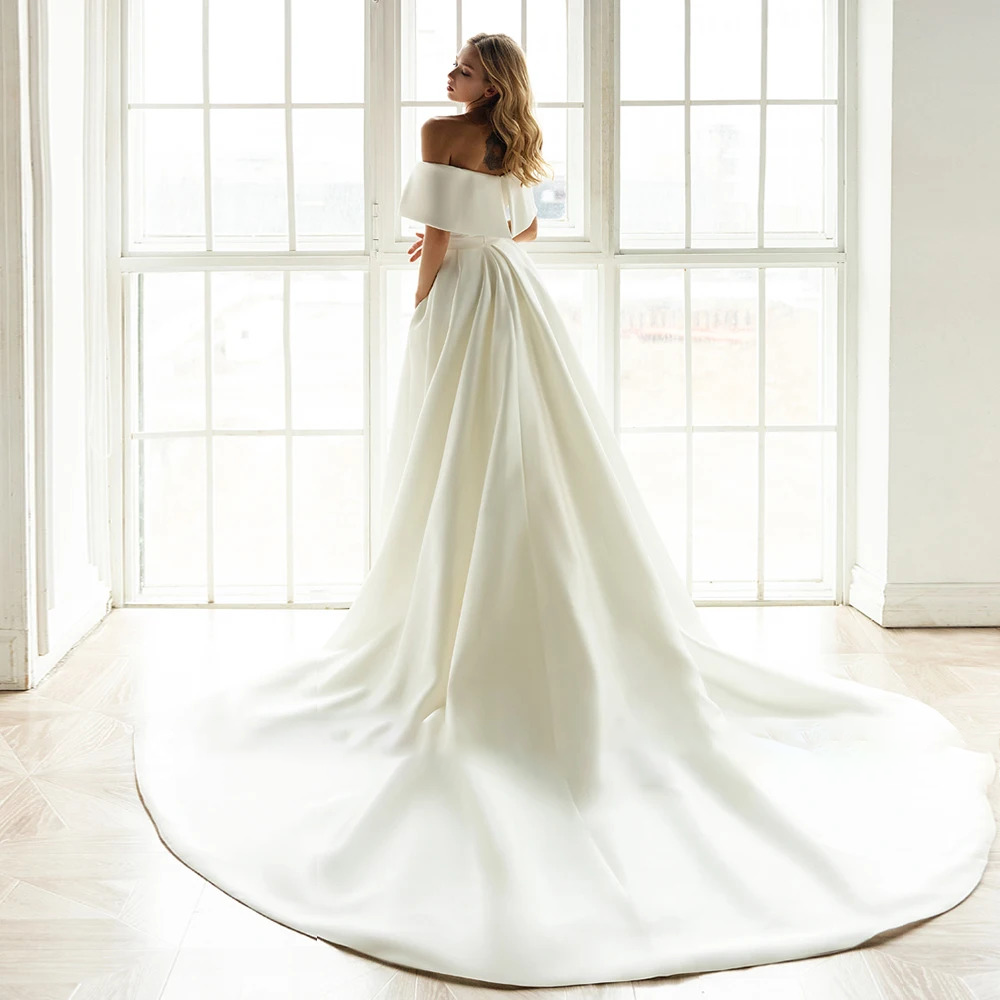 Rear profile view of a classic backless satin bridal gown emphasizing the low straight open back and a grand cascading detachable cathedral train layout.