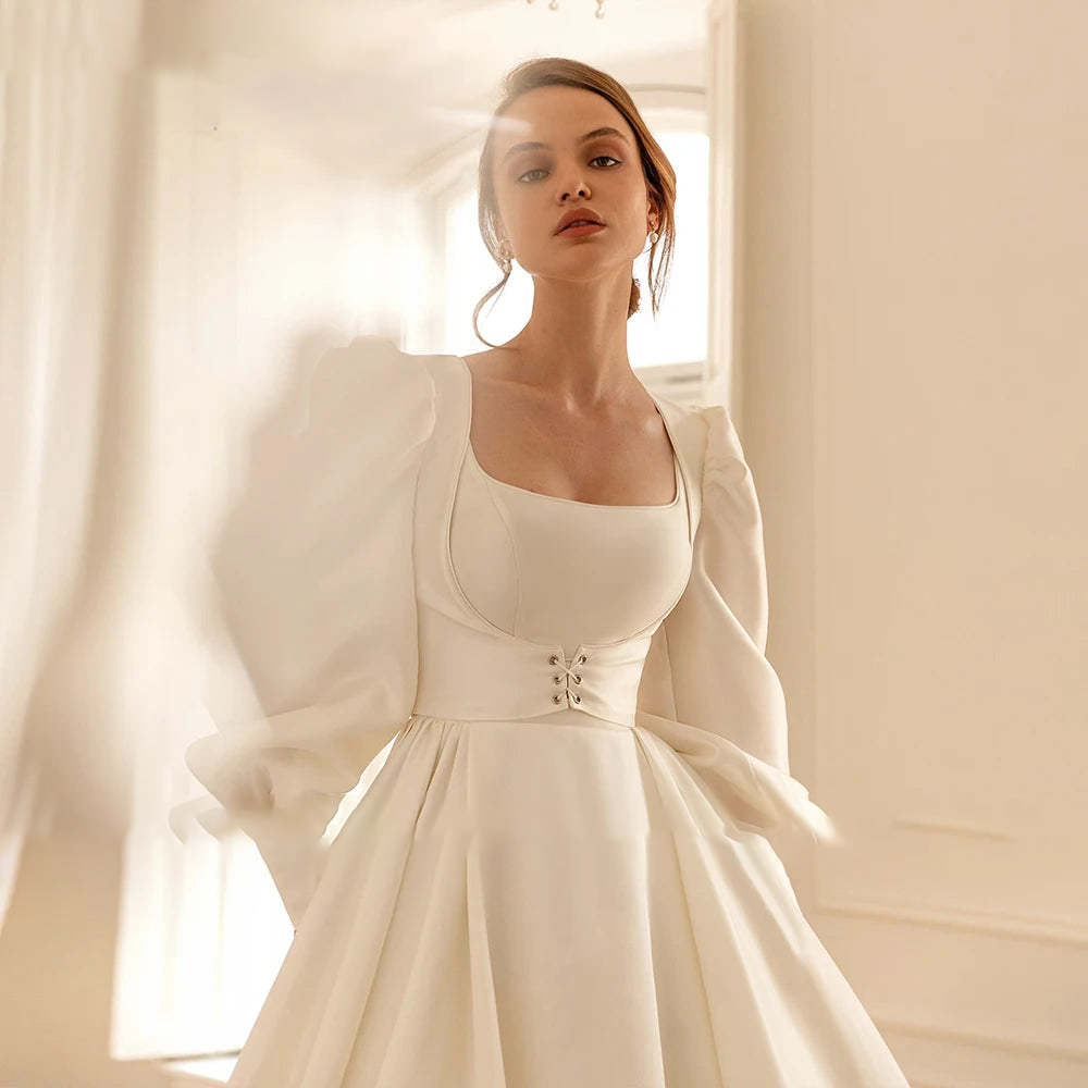 A bride posing in a luxurious ivory A-line wedding dress with long puff sleeves and an elegant corset waist detail.