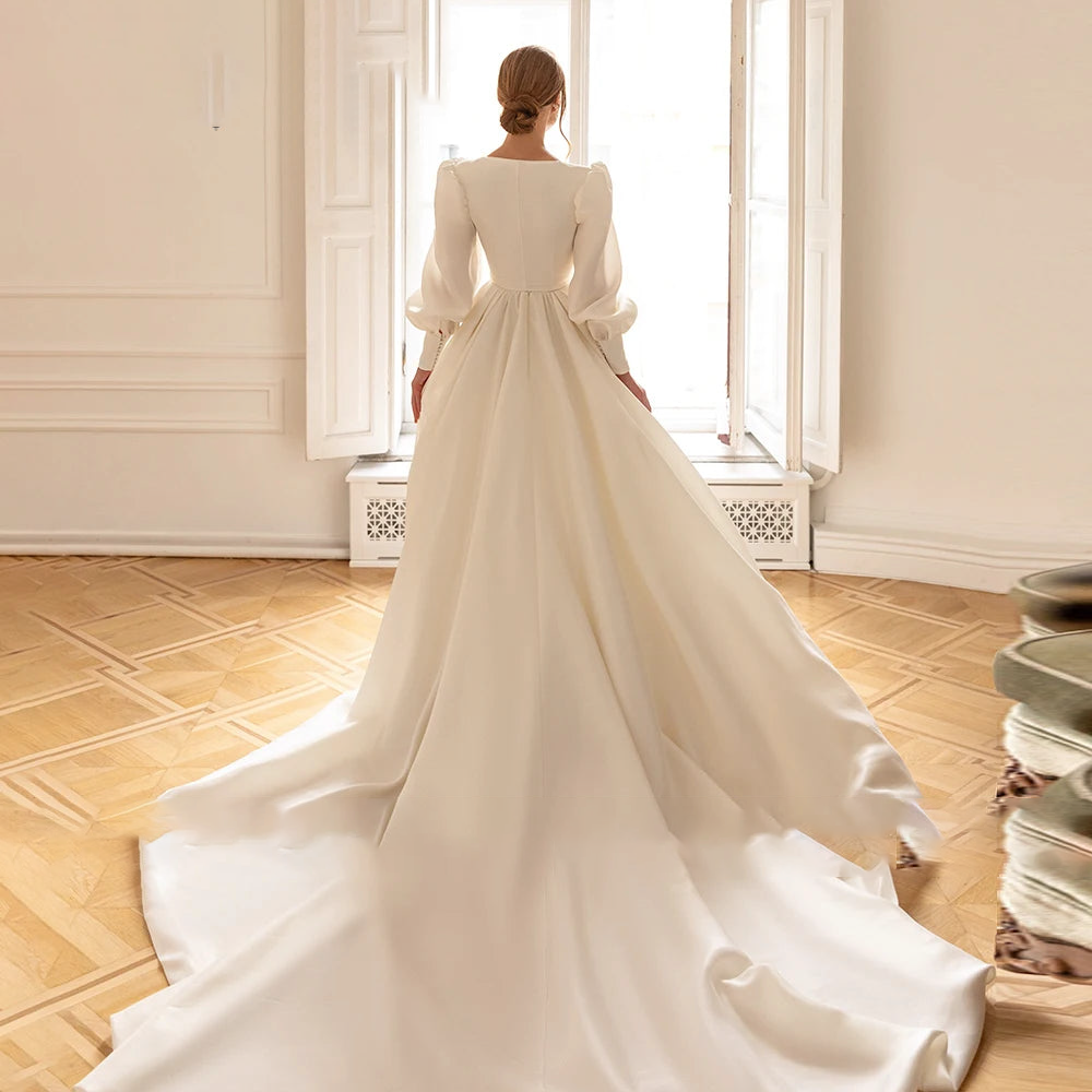 A back view of an elegant, long-sleeve ivory A-line wedding dress featuring a dramatic, flowing train.