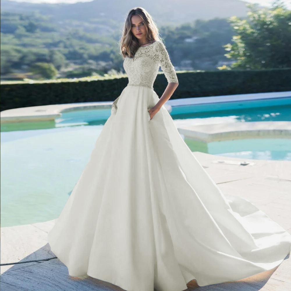 A luxurious scoop neck A-line wedding dress featuring intricate lace appliques, a beaded sash, and a flowing court train, modeled outdoors by a pool.