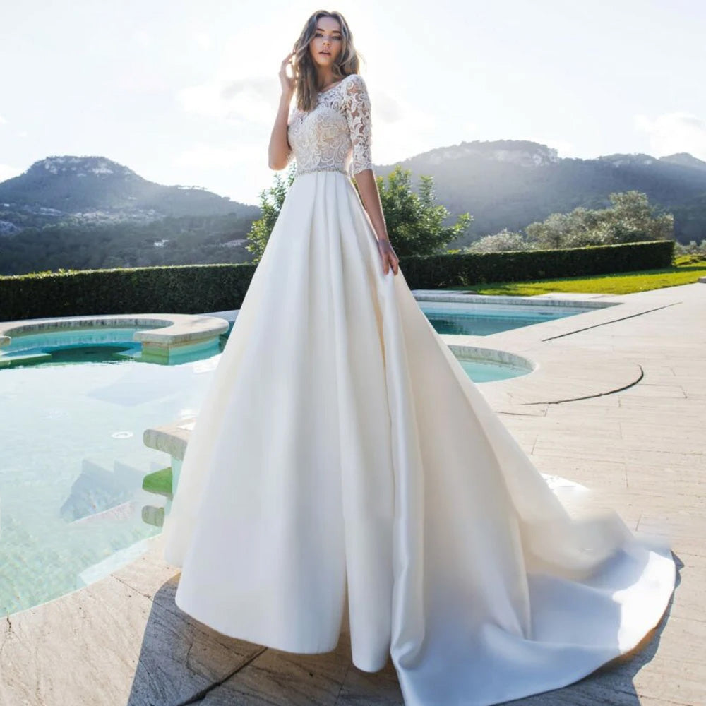 A full-length view of a scoop neck A-line wedding dress featuring intricate appliques and a court train, posed gracefully in a scenic outdoor setting.