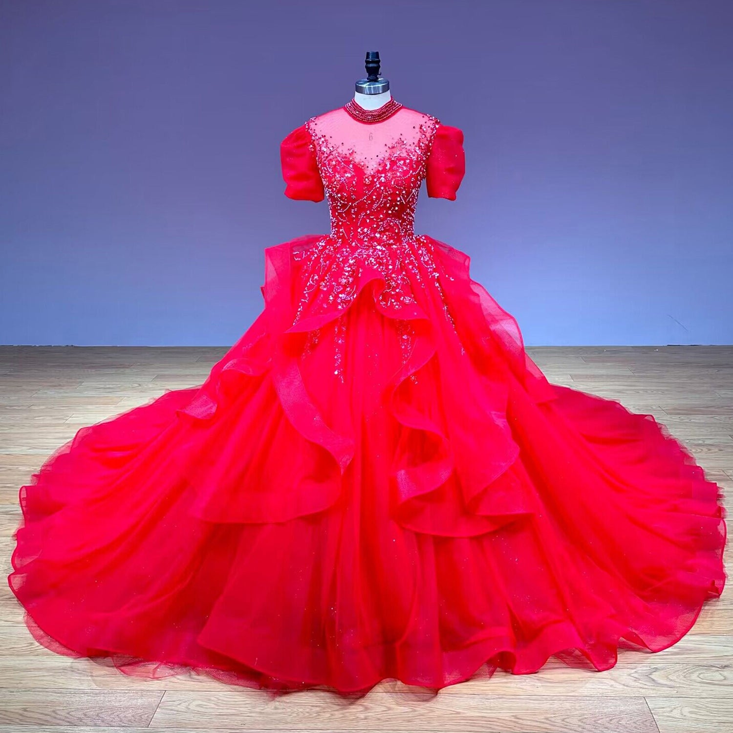 Full-length front view of a red sequin ball gown wedding dress displayed on a mannequin in a bright bridal showroom corridor.