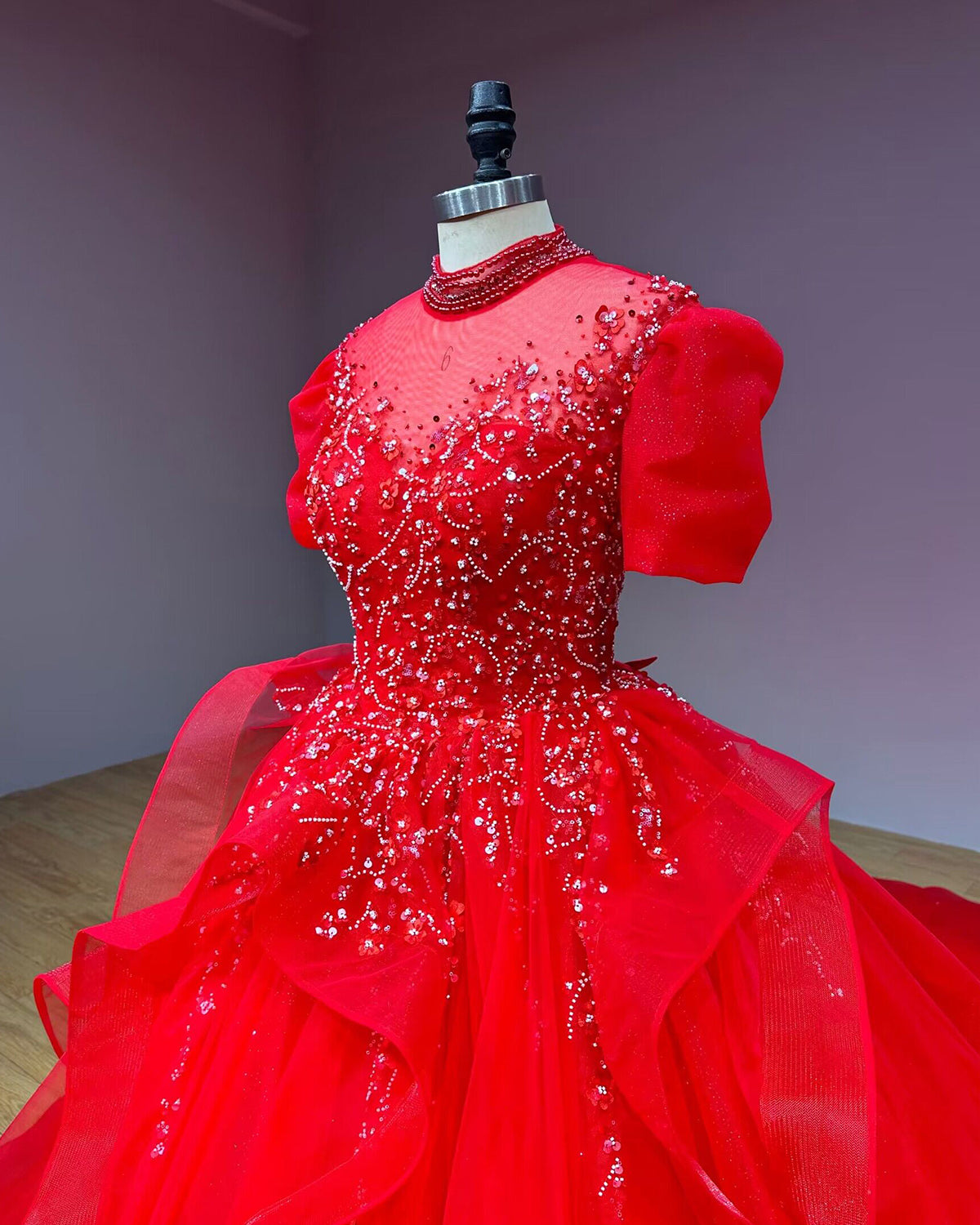 Three-quarter side view of a red sequined bridal bodice on a mannequin, emphasizing the volume of the short puff sleeves and the high sheer collar.