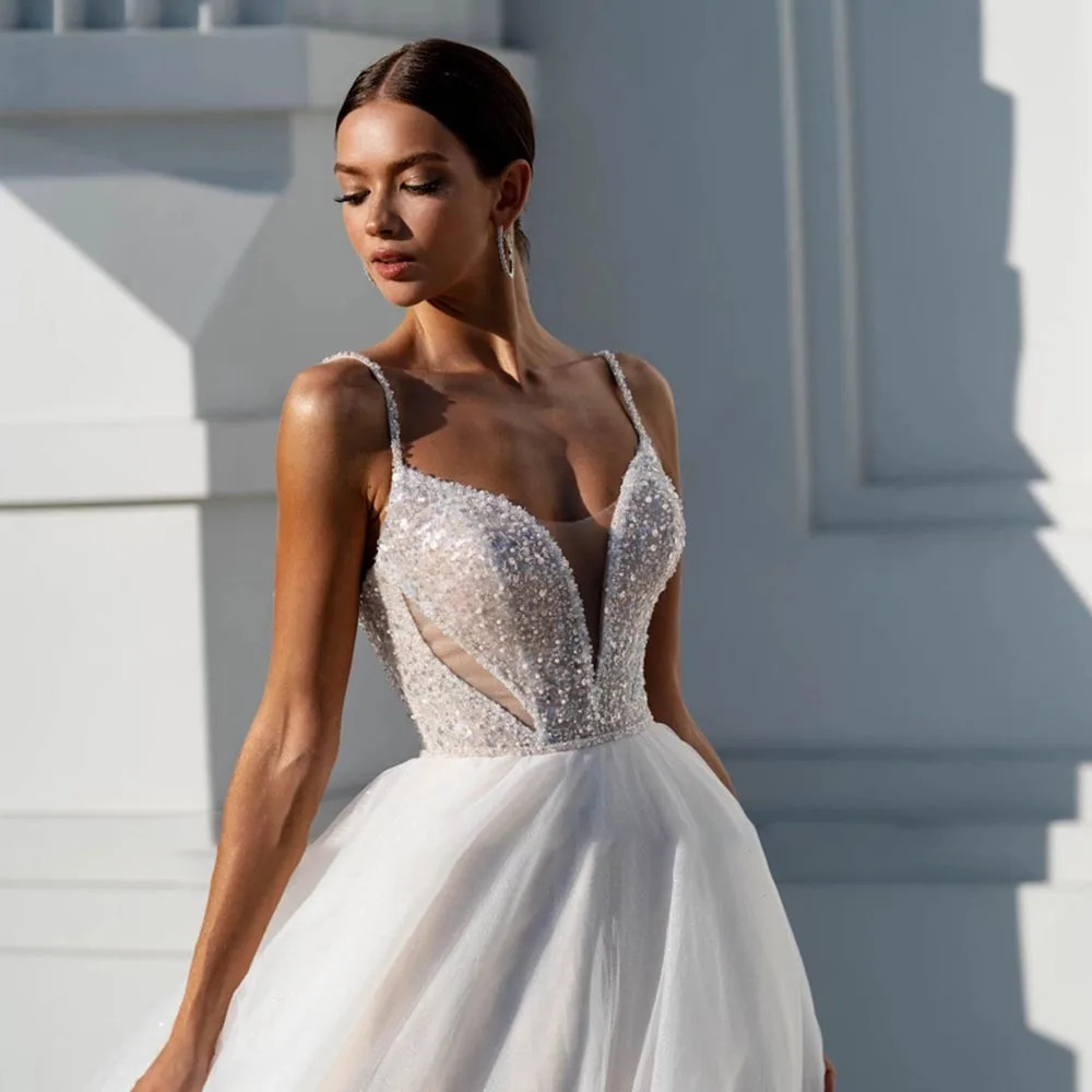 Close-up front view of a glittering princess bridal bodice with textured sequin embroidery, thin beaded straps, and a plunging V-neckline.