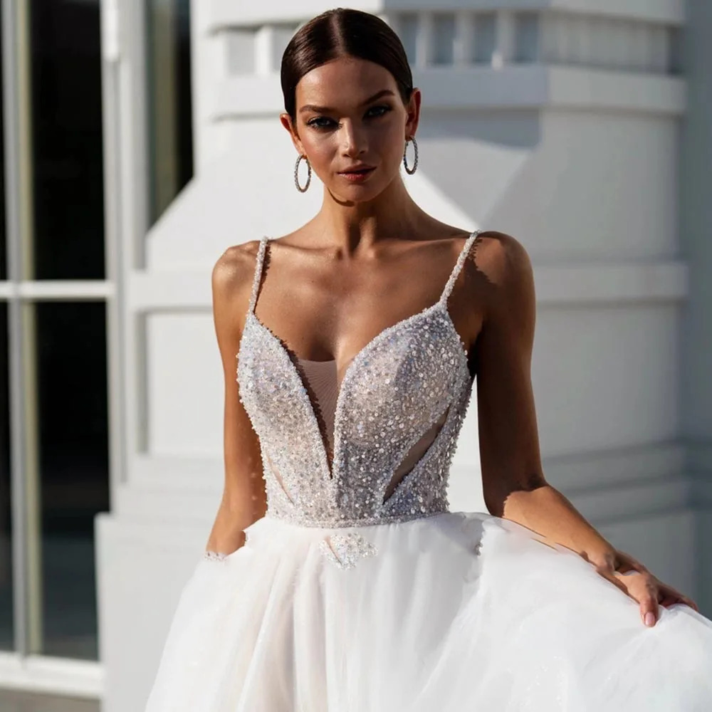 Glamorous A-line wedding dress featuring a heavily sequined glitter bodice, a deep plunging sweetheart neckline with sheer mesh, and a flowing tulle skirt.