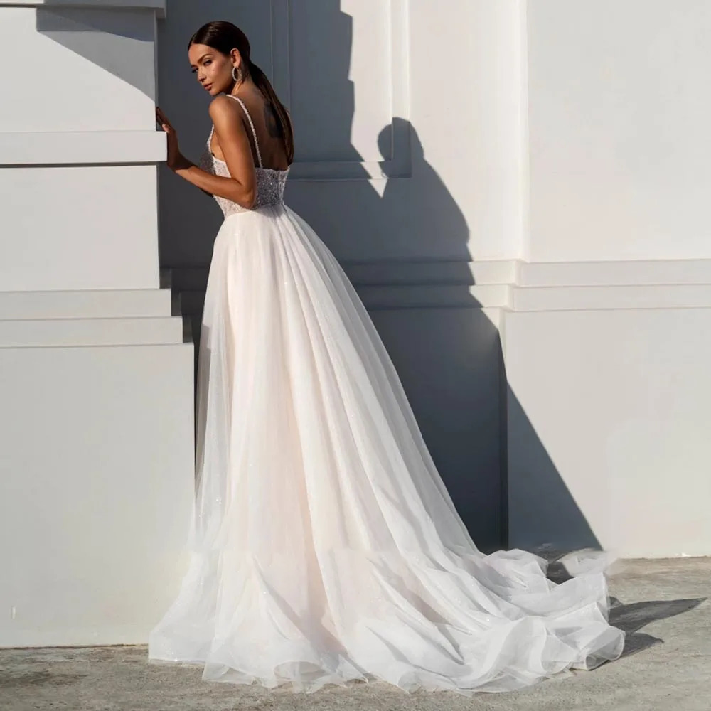 Side angle of a romantic sequined tulle wedding dress showcasing a sweeping chapel-length glitter train against a minimalist white architectural wall.