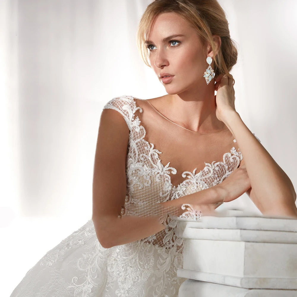 Close-up portrait of a bride modeling a luxury vintage-inspired A-line wedding dress with intricate lace appliques and long sleeves.