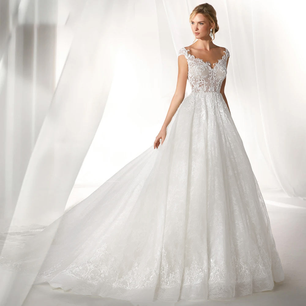 A studio shot of a bride posing in a luxury A-line bridal gown, highlighting the detailed lace long sleeves and the classic, princess-style silhouette.