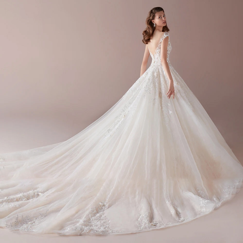 A rear view of an A-line wedding dress, showcasing the open-back design, floral lace appliques, and an elegant, sweeping chapel train.