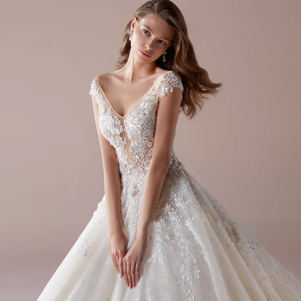 A close-up shot of the bodice of a V-neck A-line bridal gown, emphasizing the intricate floral lace work and cap sleeve design.