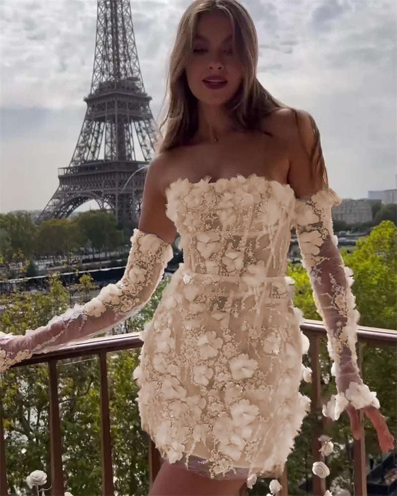 A model on a balcony wearing a champagne-toned strapless mini wedding dress with 3D floral lace appliques and detachable long lace sleeves, with the Eiffel Tower visible in the distance.