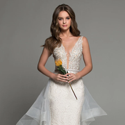 A model wearing a shimmering, beaded V-neck mermaid wedding dress with a detachable train, holding a yellow flower.