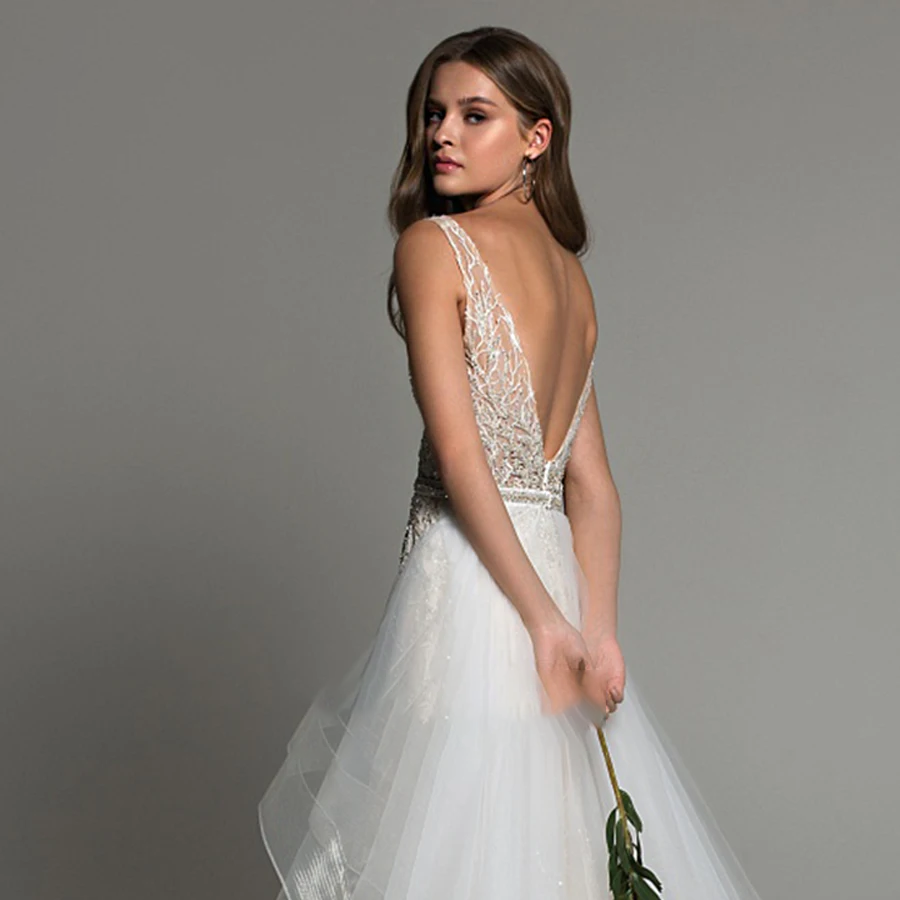 A back view of a sleeveless, backless mermaid bridal gown featuring intricate shimmering beadwork and a detachable train.