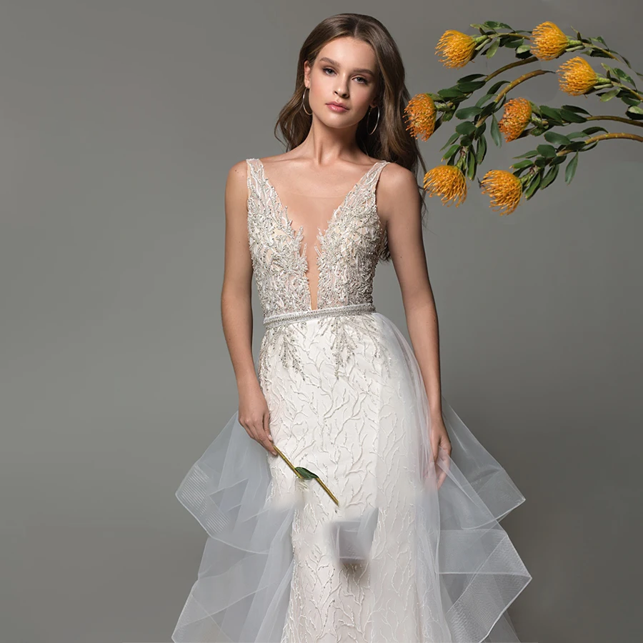 A close-up of a bride in a shimmering V-neck mermaid wedding gown with beaded details, accented by floral decor.