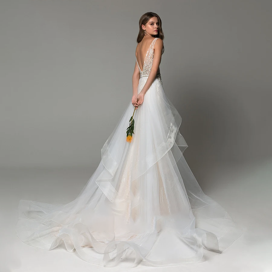 A bride posing in a backless mermaid wedding dress with shimmering beading and a detachable train, holding a single yellow flower.