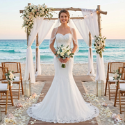 Bride wearing a sexy strapless mermaid wedding dress with intricate lace detailing, posing at a beach wedding ceremony.