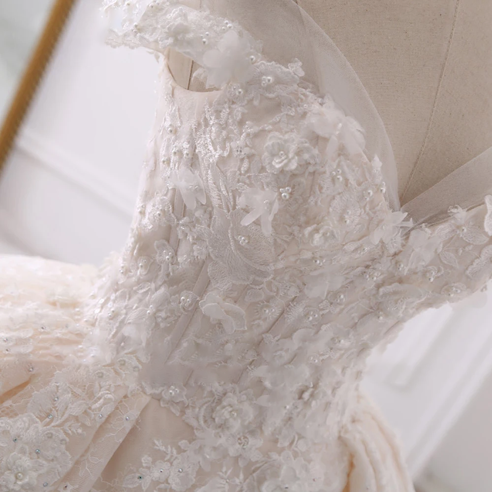 Detailed close-up of a bridal gown bodice, highlighting the intricate floral embroidery, pearl beadwork, and layered applique texture.