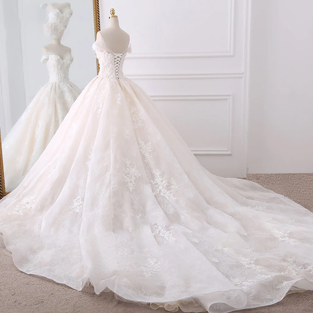 Full studio view of an elegant ball gown wedding dress from the back, displaying the voluminous tulle skirt, lace-up corset, and chapel train.