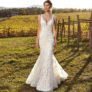 A beautiful bride standing in a golden vineyard wearing a sexy, sleeveless mermaid wedding dress with intricate lace appliques and a deep V-neck.
