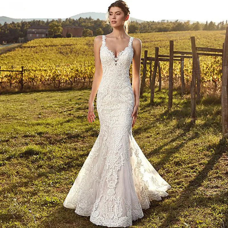 A beautiful bride standing in a golden vineyard wearing a sexy, sleeveless mermaid wedding dress with intricate lace appliques and a deep V-neck.