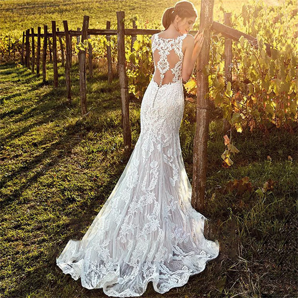 Back view of a stunning lace mermaid bridal gown, featuring a dramatic illusion back, button detailing, and a sweeping train in a scenic vineyard.