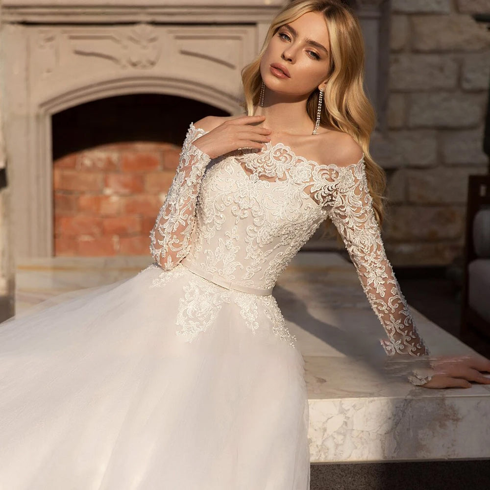Close-up of a model wearing a long-sleeved, off-the-shoulder vintage wedding dress featuring intricate lace appliqué detailing on the bodice and sleeves.