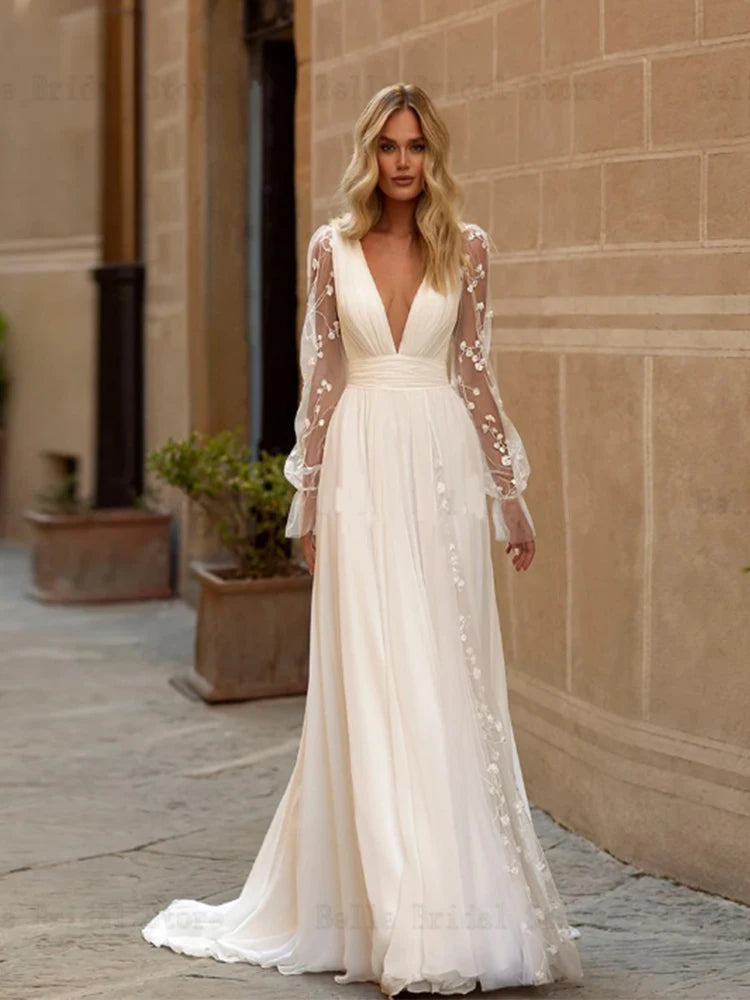 Elegant A-line wedding dress with a deep V-neck and sheer long sleeves, detailed with floral appliques and a flowing sweep train.