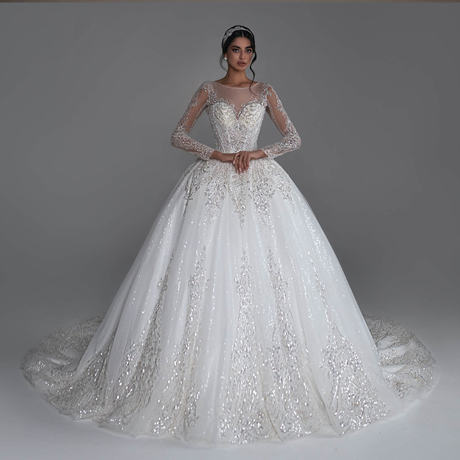 A high-fashion bridal model posing in a sparkly long sleeve ball gown wedding dress with heavy silver sequined beading and a sheer illusion neckline.