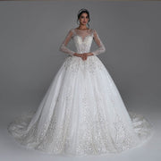A high-fashion bridal model posing in a sparkly long sleeve ball gown wedding dress with heavy silver sequined beading and a sheer illusion neckline.