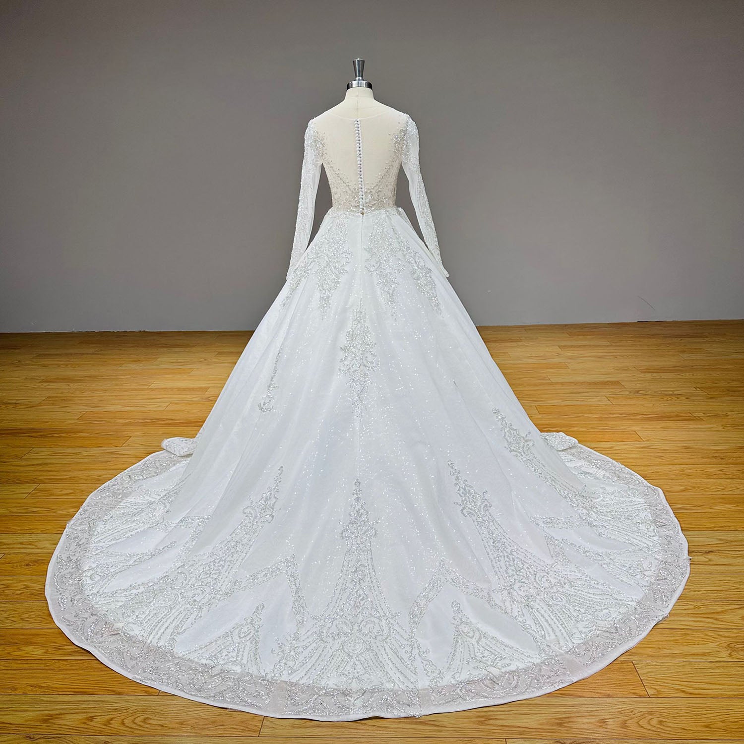 Full back display of a shining sequined ball gown wedding dress on a mannequin, highlighting the sweeping cathedral train with an intricate glitter border pattern.