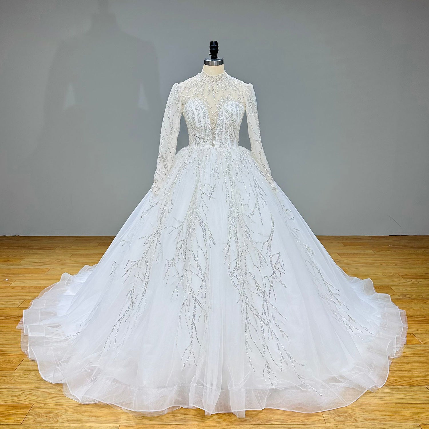 Standard front view of a shining high neck long sleeve luxury ball gown bridal dress on a grey studio backdrop.
