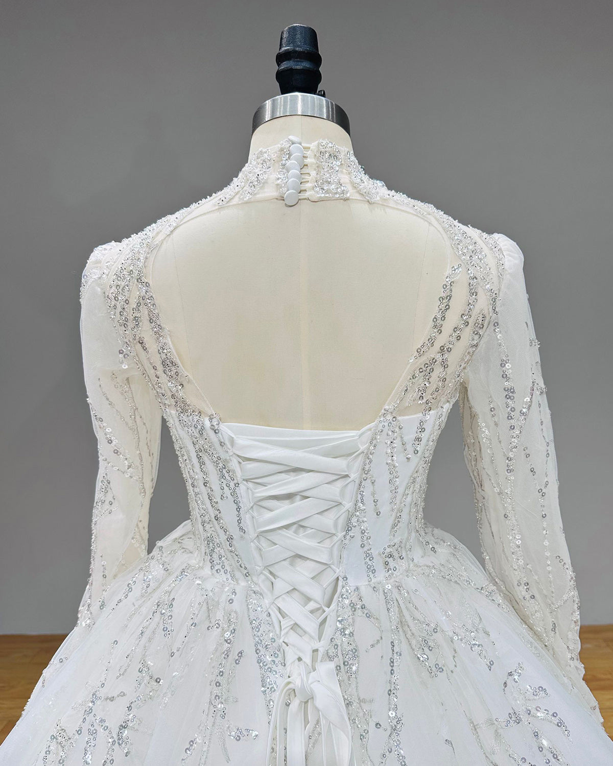 Back close-up of a luxury wedding gown showcasing a high neck button closure, sheer keyhole cutout, and lace-up corset.