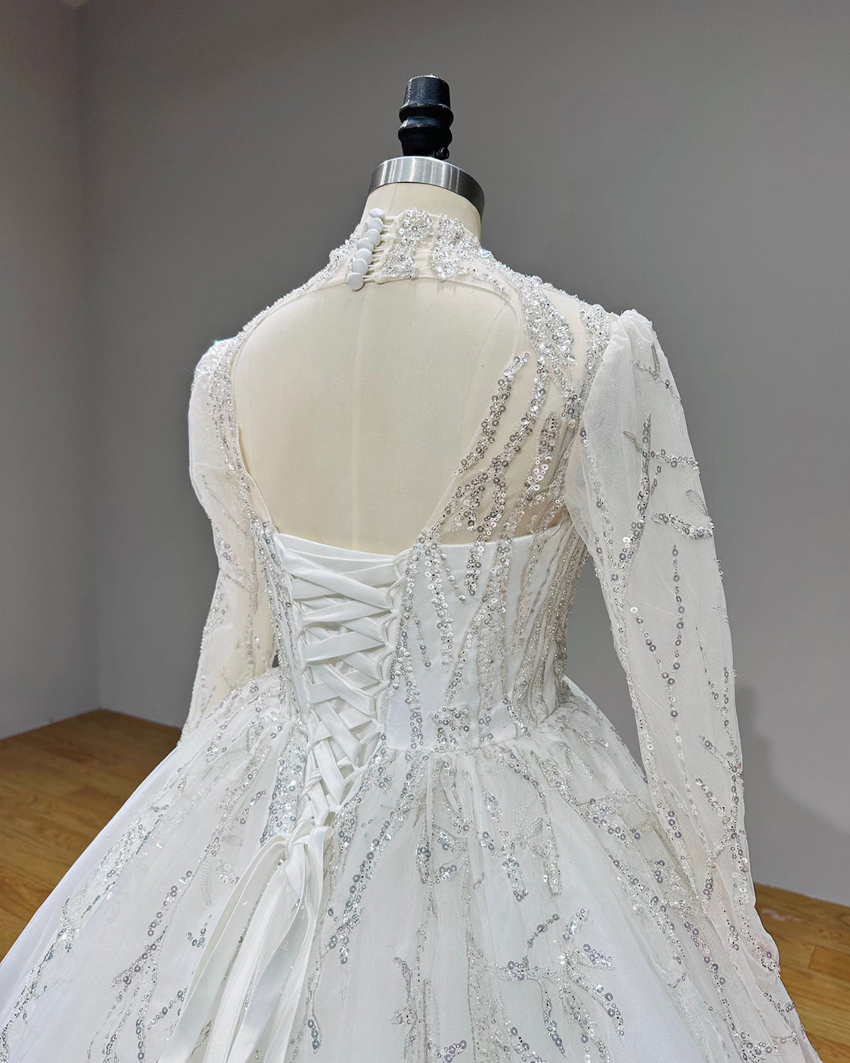 Angled back view of a bridal dress bodice highlighting a modern keyhole back, structured corset strings, and sequined sleeves.