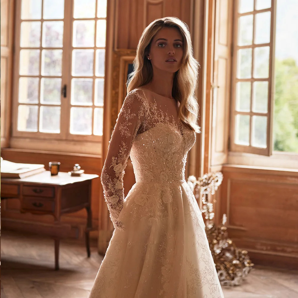 Glamorous long sleeve bridal dress featuring a sweetheart neckline lining under sheer mesh, heavily embellished with reflective crystals and beads.