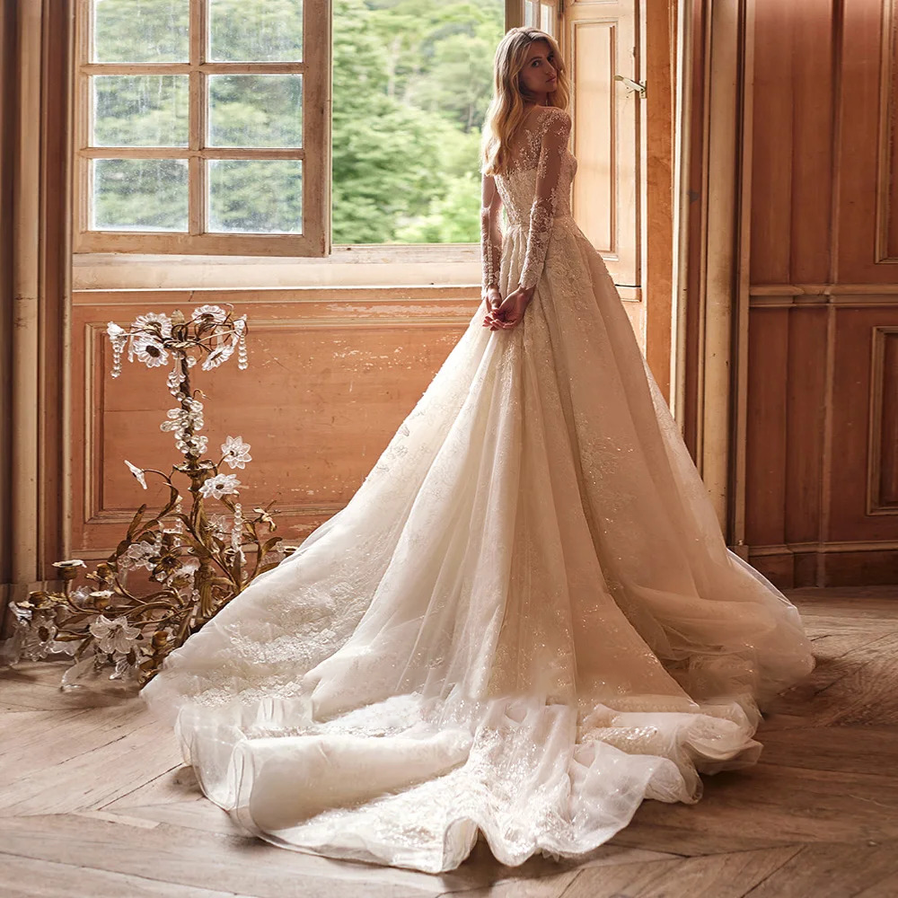Grand rear view of an illusion back wedding dress showing the magnificent length of a glittering cathedral tulle train spread across an indoor wooden floor.