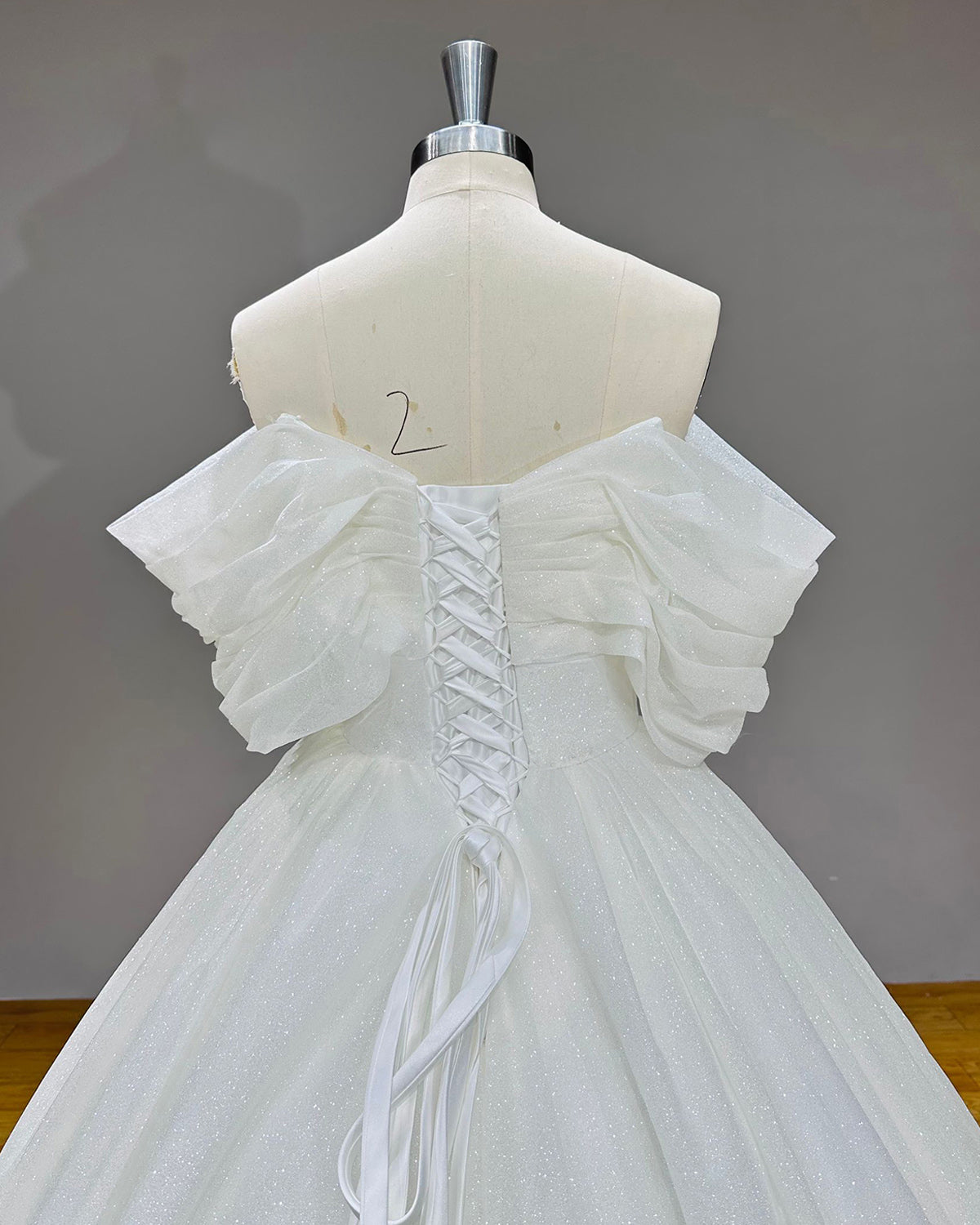 Detailed close-up back view of the shimmering bridal gown bodice highlighting the adjustable lace-up corset closure and gathered off-the-shoulder tulle sleeves.