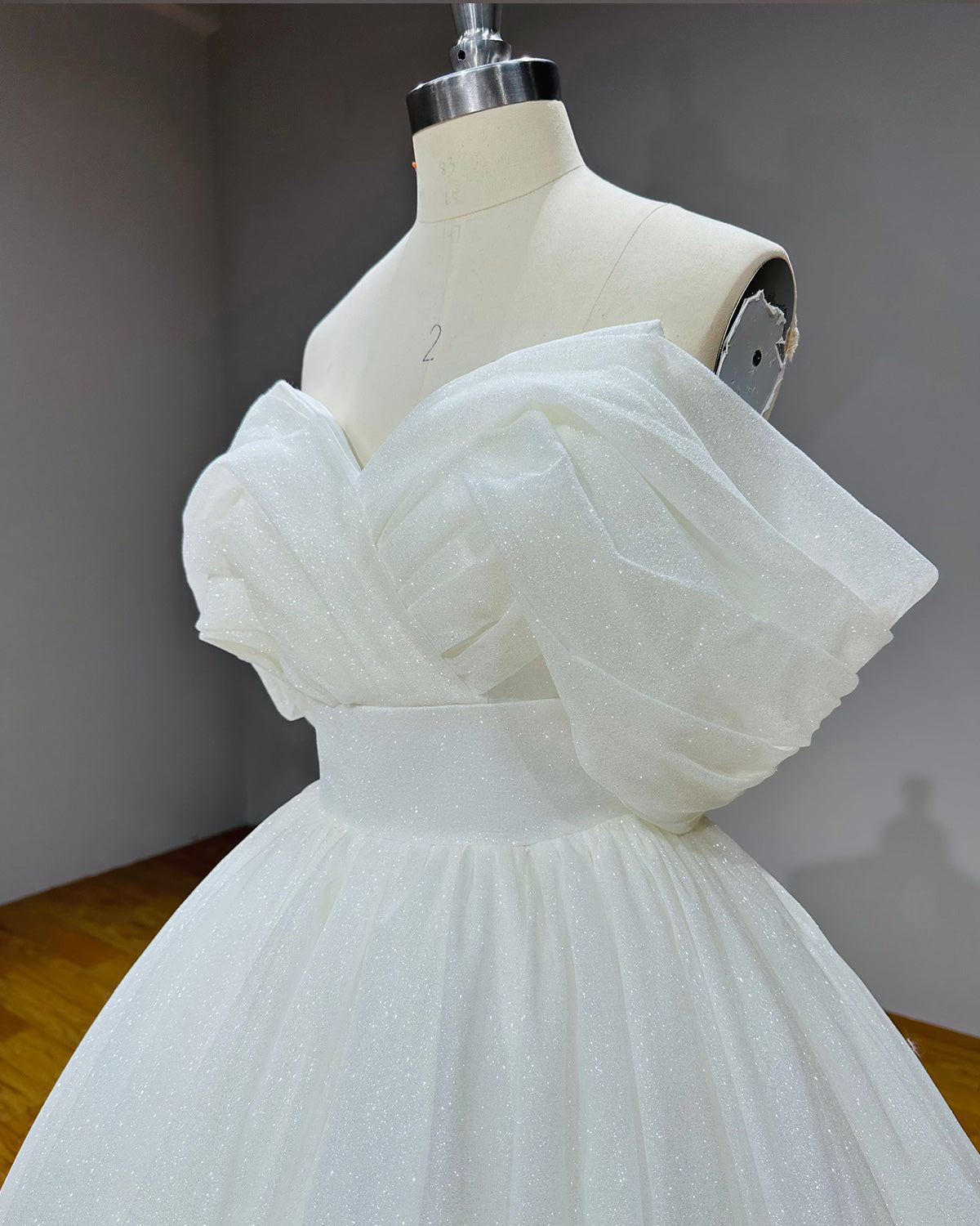 Close-up side angle of the wedding dress bodice showcasing the elegant pleated crossover portrait neckline and reflective glitter tulle fabric.