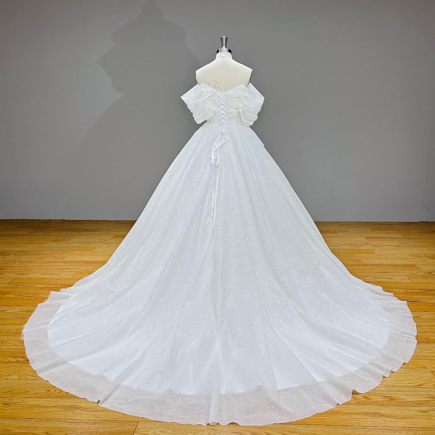 Full-length studio view of the back of the sparkling bridal gown on a mannequin, emphasizing the lace-up corset back and a dramatic, wide glitter train.